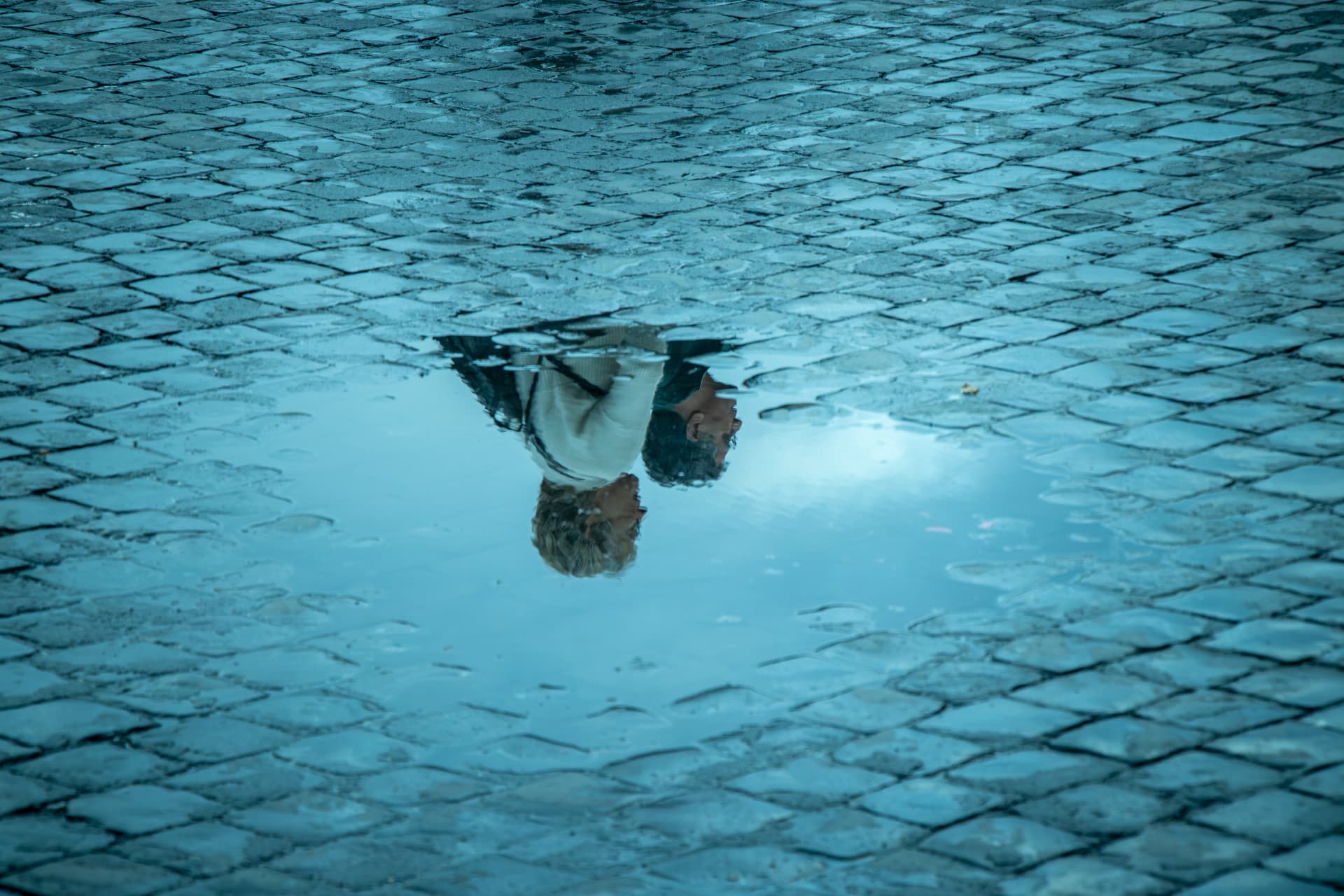 Reflection of a passer-by in a puddle on cobblestones