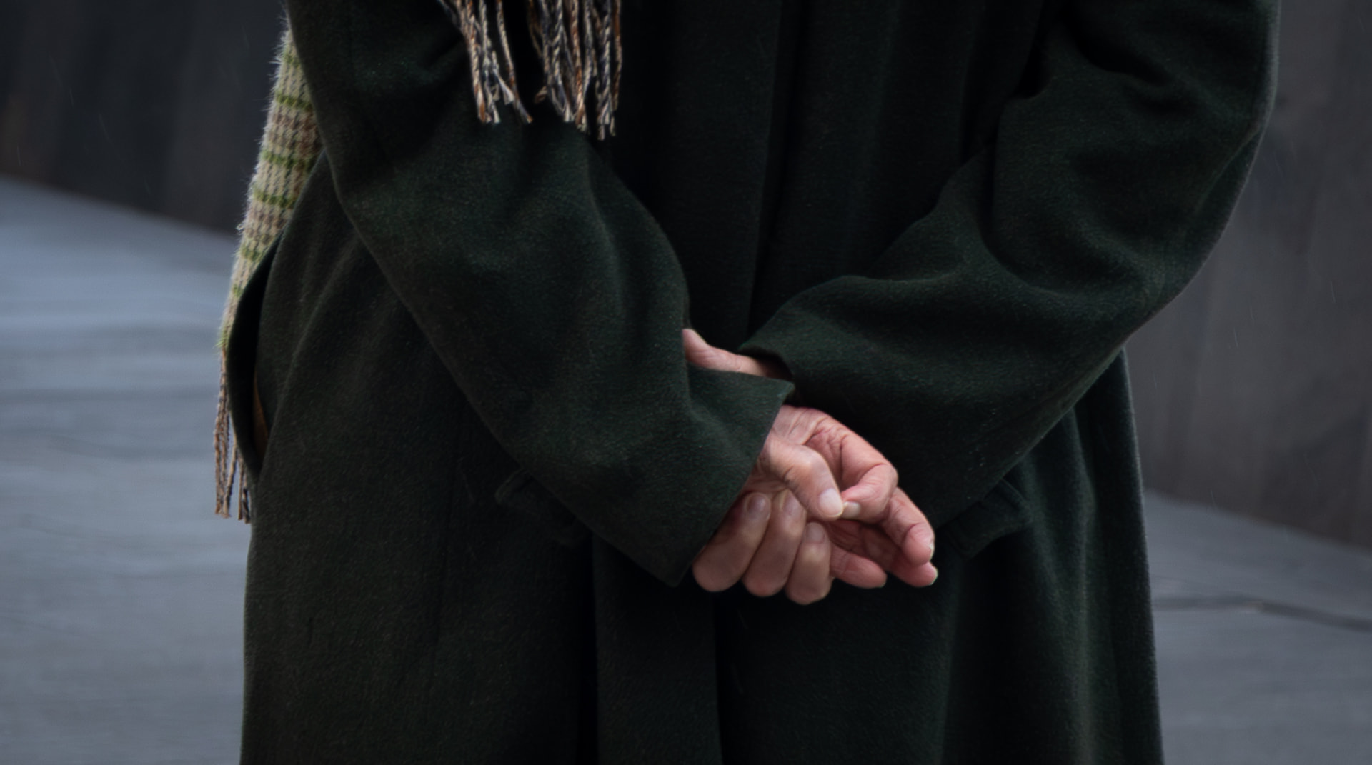 Hands clasped behind a wool coat